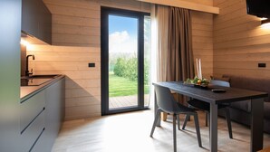 A modern kitchen with a built-in oven, a dining area with a table and chairs, and a sliding glass door leading to a garden. - The Village Chalet (Castel di Sangro)