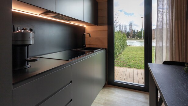 A modern kitchen with a built-in coffee maker, a window with a view of a deck and greenery, and a sliding glass door. - The Village Chalet (Castel di Sangro)