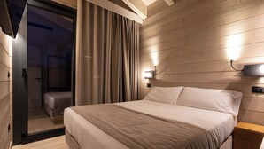 A modern bedroom with a large bed, wooden panel walls, a sliding glass door, and a nightstand with a lamp. - The Village Chalet (Castel di Sangro)