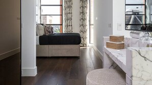A modern bedroom with a bed, a small seating area, a marble vanity, and large windows. - Modern 3-bed Residence in Westminster With Concierge (London)