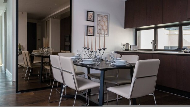 A modern dining area with a dark wooden table set for six, surrounded by white chairs. There are framed artworks on the wall above the table. - Modern 3-bed Residence in Westminster With Concierge (London)