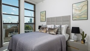 A modern bedroom with a large bed, a city view, and artwork on the walls. - Modern 3-bed Residence in Westminster With Concierge (London)