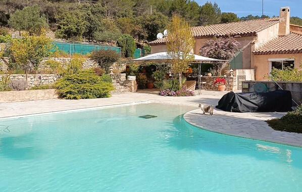 A swimming pool with a stone border, surrounded by a garden with various plants and a stone wall. - MAISON AVEC PISCINE 1 (Solliès-Toucas)
