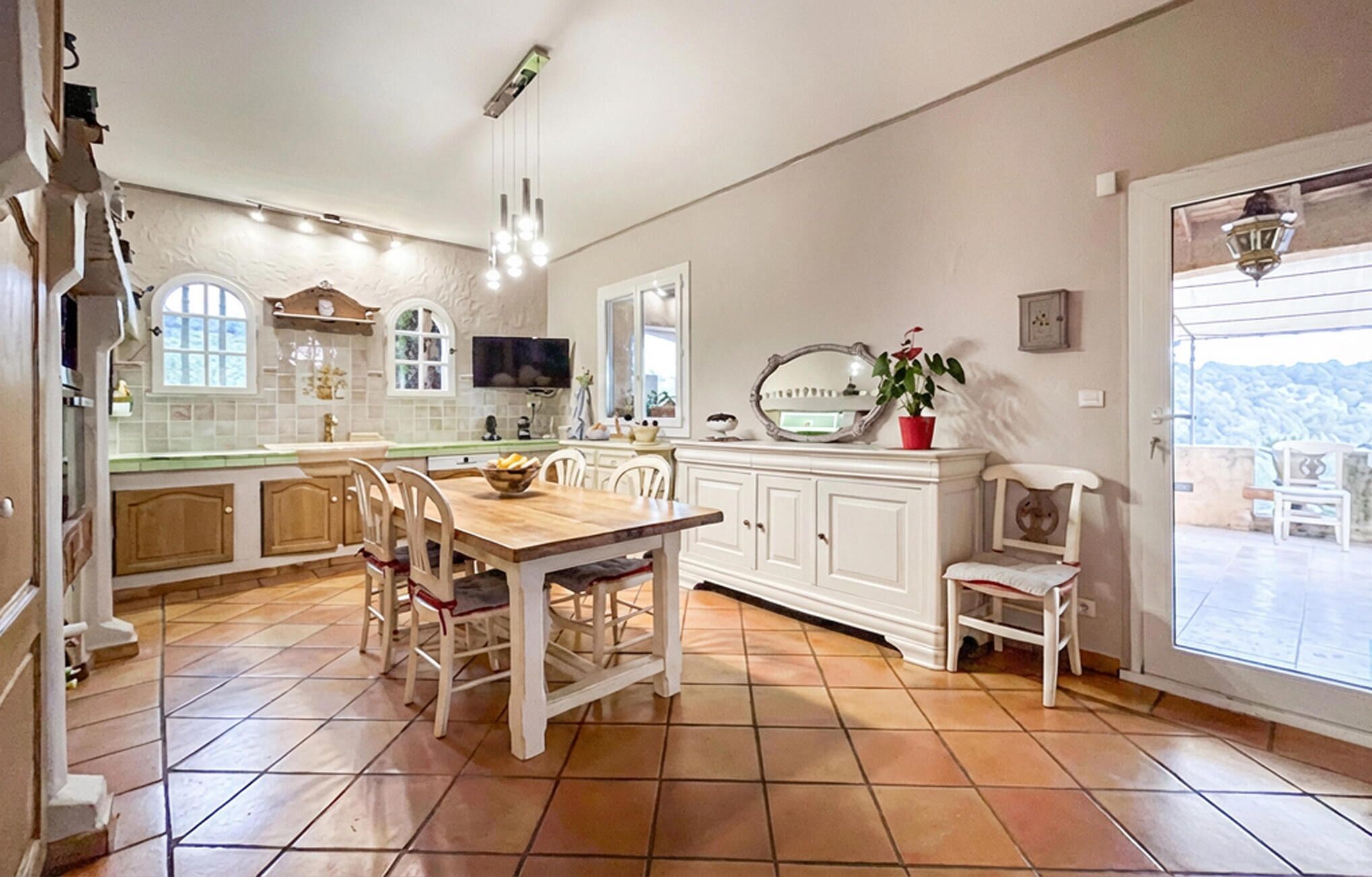 A spacious kitchen with a wooden dining table, white cabinetry, and a large window offering a view.