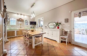 A spacious kitchen with a wooden dining table, white cabinetry, and a large window offering a view. - MAISON AVEC PISCINE 1 (Solliès-Toucas)