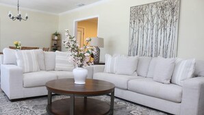 A living room with a beige sectional sofa, a round coffee table, a patterned rug, a wall-mounted lamp, and a large abstract painting. - Welcome to University Place (Ruston)