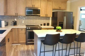 Une cuisine moderne avec des meubles en bois, un réfrigérateur en acier inoxydable, un four encastré et un grand îlot central doté de tabourets de bar.