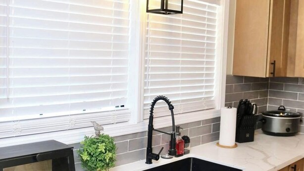 A kitchen with a double sink, wooden cabinets, a black microwave, and a hanging light fixture. - Welcome to University Place (Ruston)