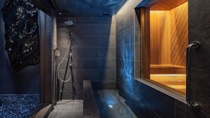Een moderne badkamer met een douchecabine van glas, donkere tegels en een houten bankje.
