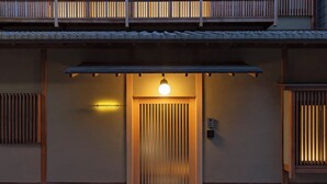 De ingang van een traditioneel Japans gebouw, met een schuifdeur, een hanglamp en een klein apparaat aan de muur.