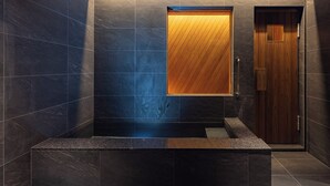 Een moderne badkamer met donkere tegels, een houten wastafelmeubel en een deur.