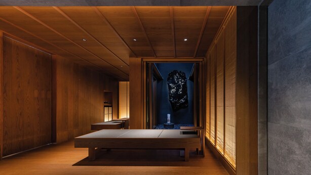 Een modern interieur met een houten bank, een wandsculptuur en een kleine waterpartij.