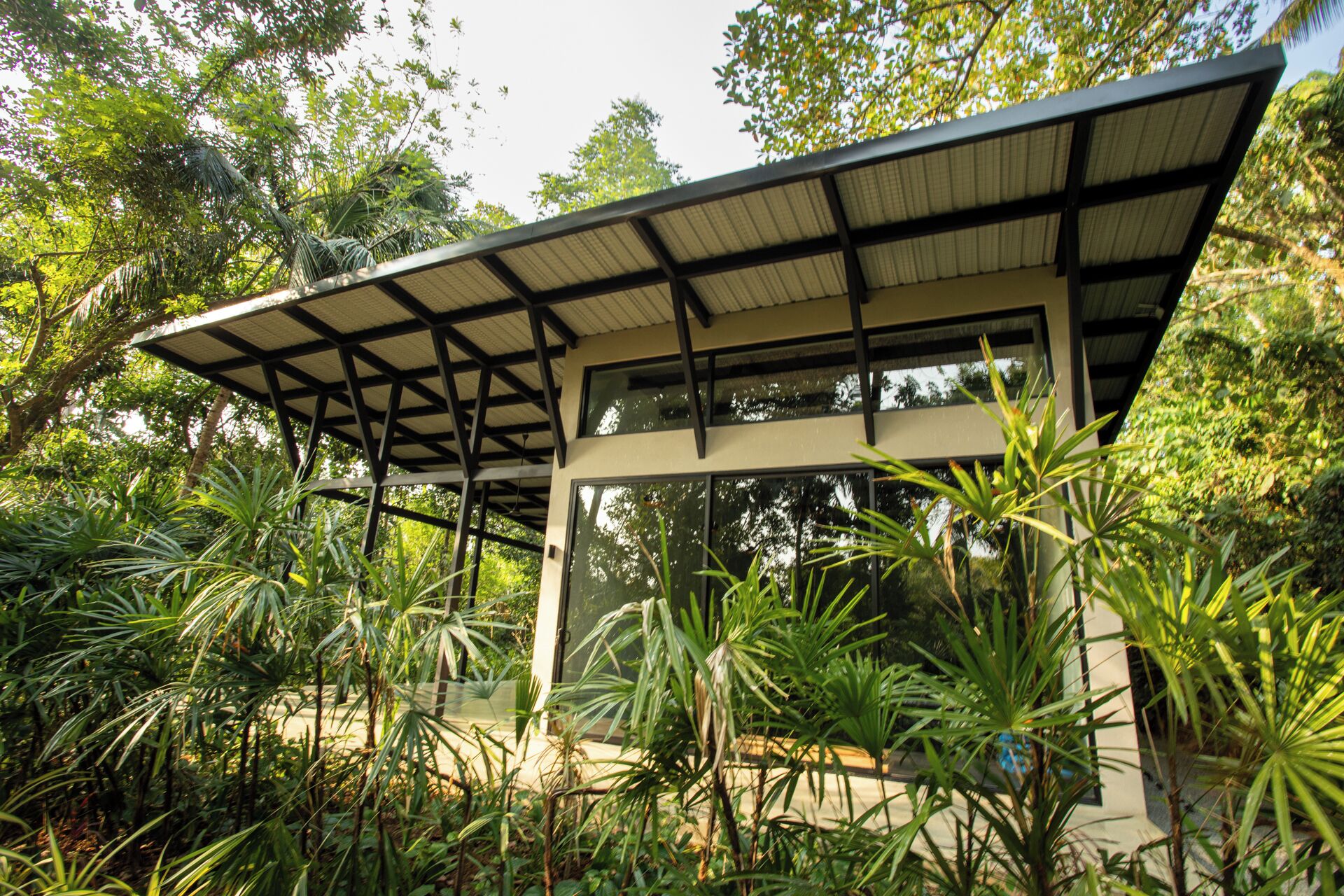 A modern pavilion with a glass enclosure, surrounded by lush tropical vegetation.