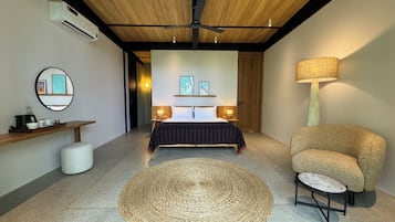 Un dormitorio con cama, mesitas de noche, un tapete redondo tejido, una silla, una lámpara, un espejo y un estante con objetos.