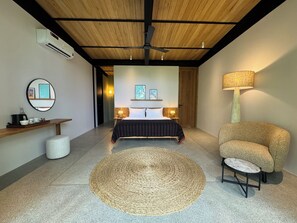 Une chambre à coucher comprenant un lit, des tables de chevet, un tapis rond en fibres tressées, une chaise, une lampe, un miroir et une étagère avec divers objets.