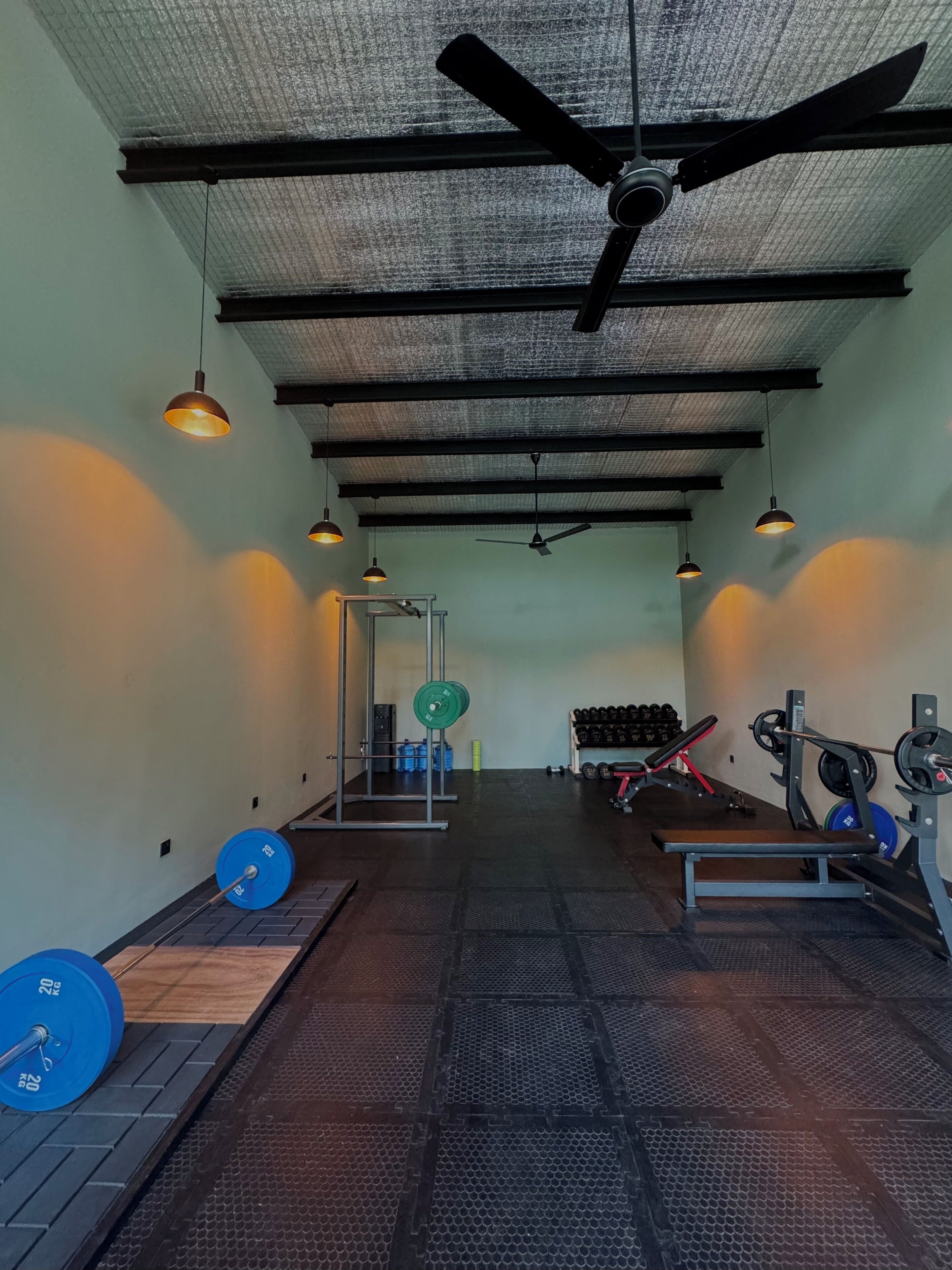 Ein Fitnessraum mit Gewichte, Bänken und einem Deckenventilator.