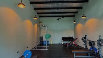 Ein Fitnessraum mit Gewichte, Bänken und einem Deckenventilator.