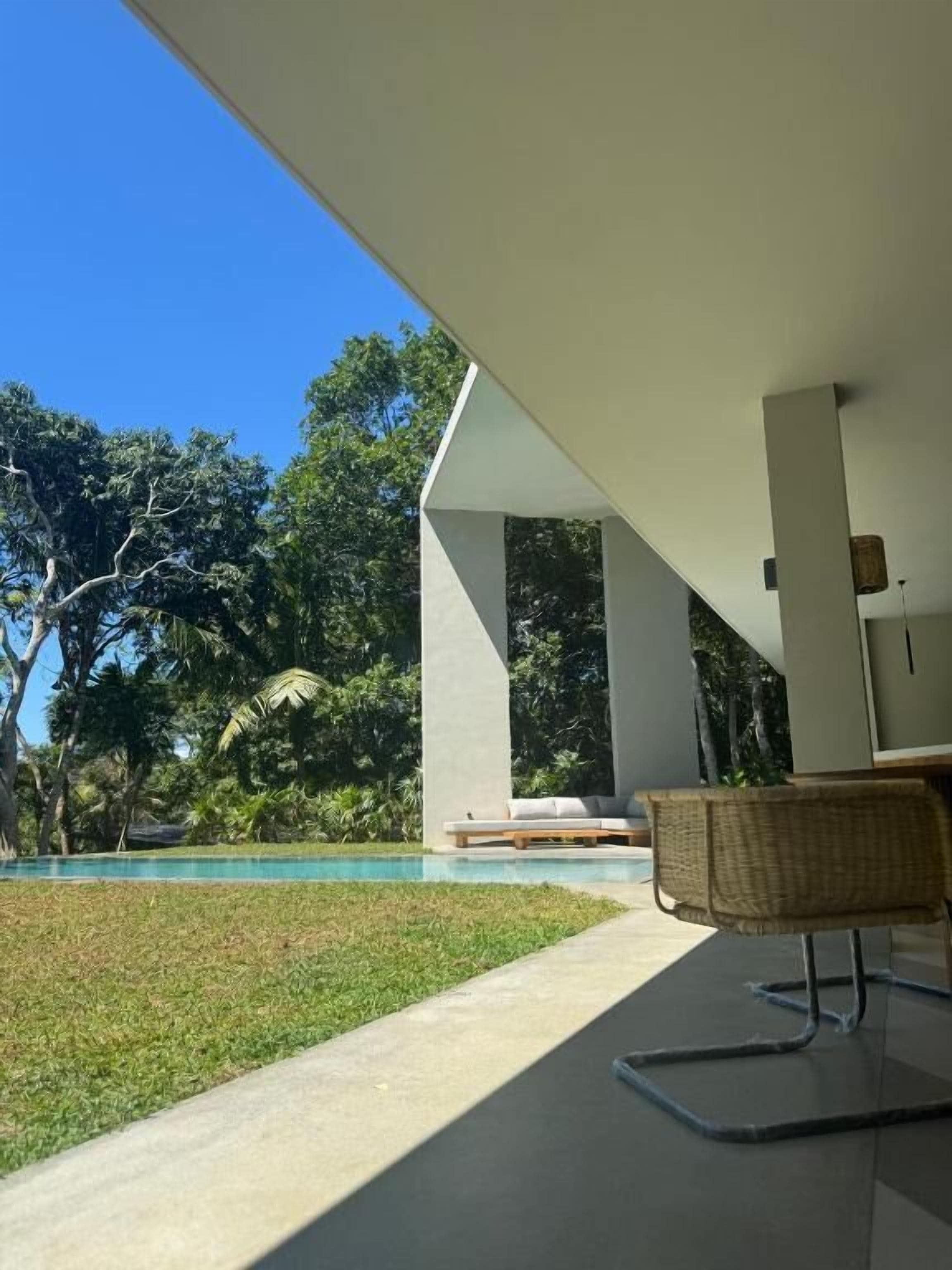 A modern outdoor seating area with a pool, surrounded by lush greenery and trees.