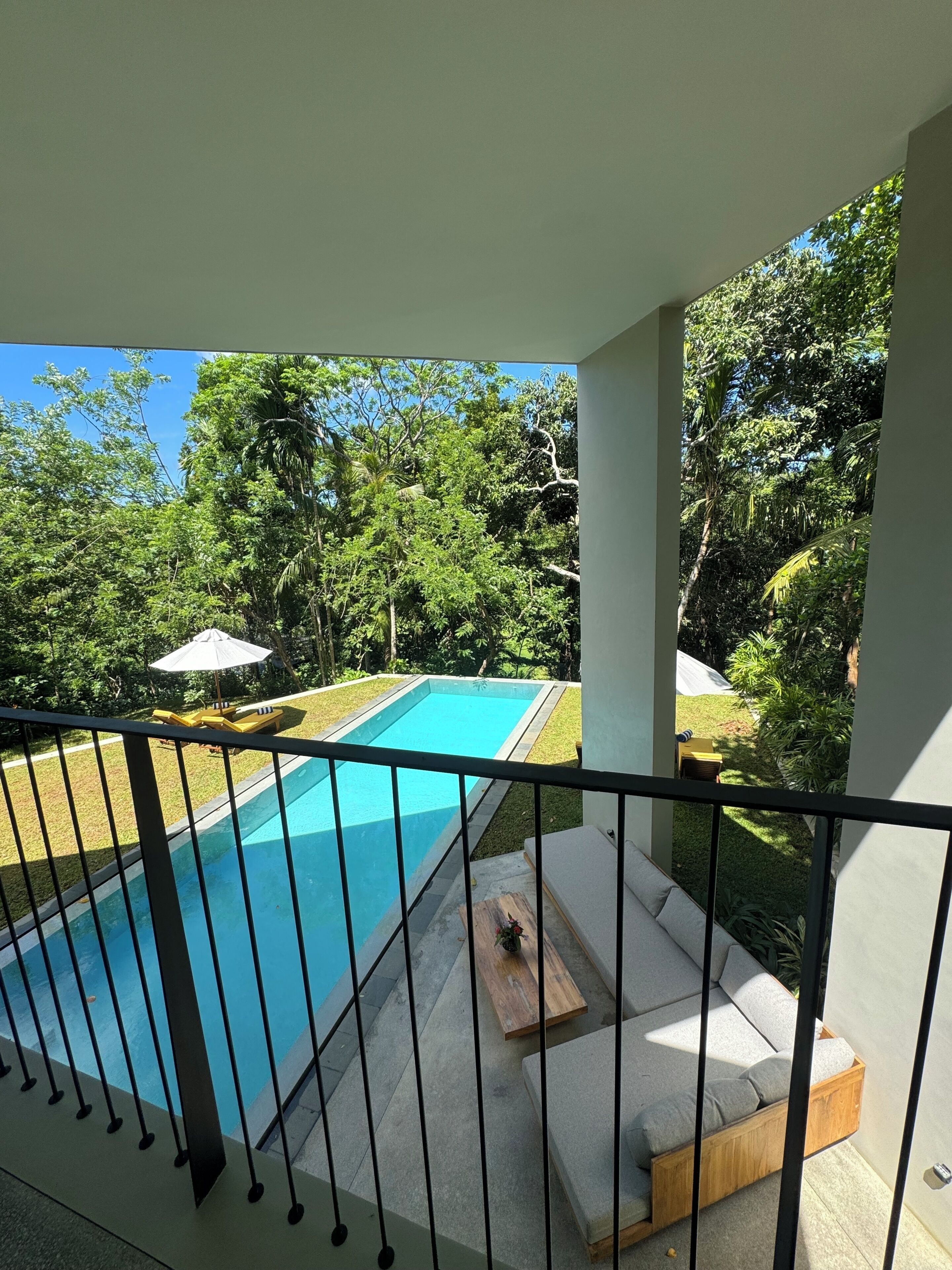 A swimming pool with a surrounding deck, a lounge area with cushions, and a view of a lush green landscape.