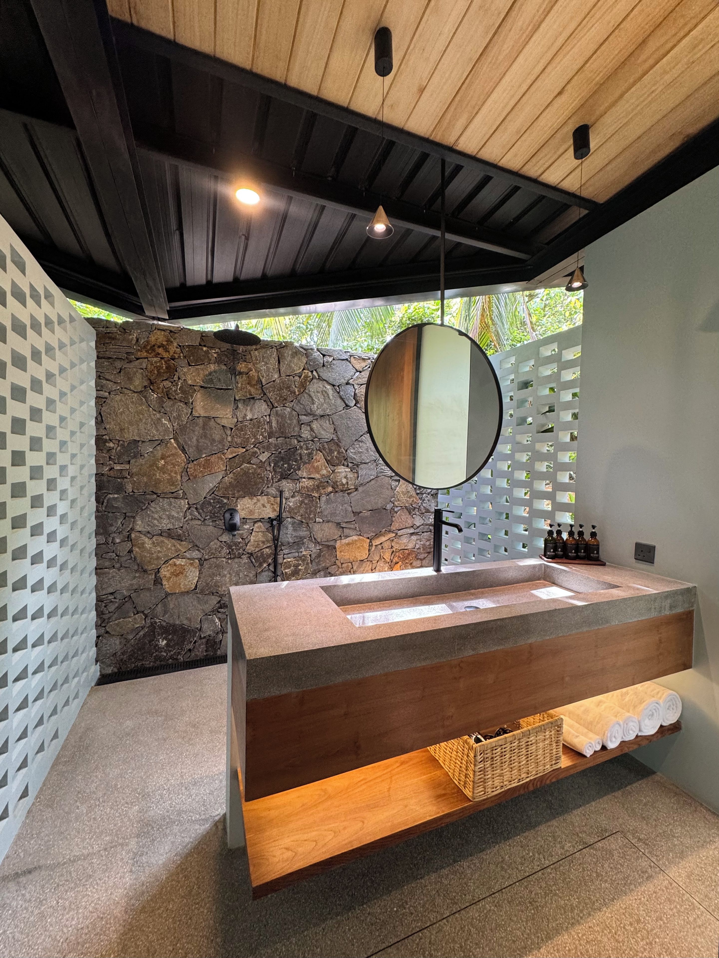 Une salle de bain moderne avec un mur en pierre, un plafond en bois, un grand miroir et un lavabo intégré.