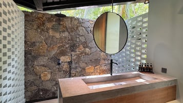 Un baño moderno con pared de piedra, techo de madera, un espejo grande y un lavamanos empotrado.