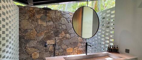 Une salle de bain moderne avec un mur en pierre, un plafond en bois, un grand miroir et un lavabo intégré.