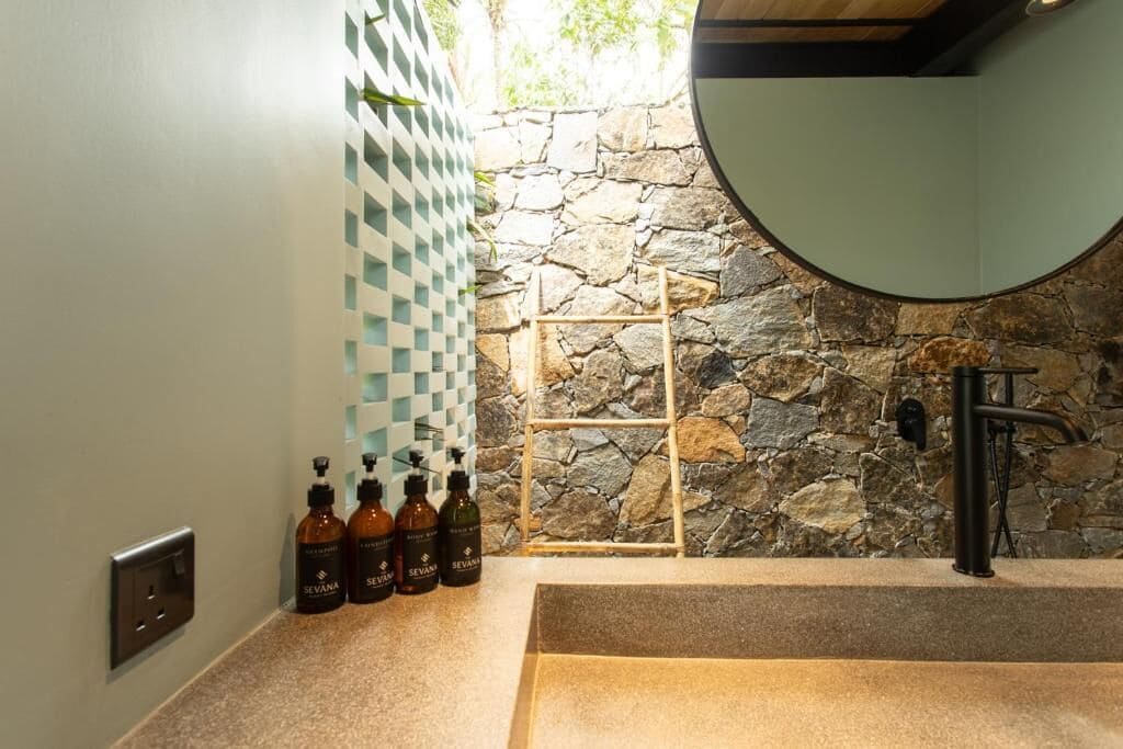 A bathroom with a stone wall, a checkered wall panel, a sink, and several bottles of Sevana products.