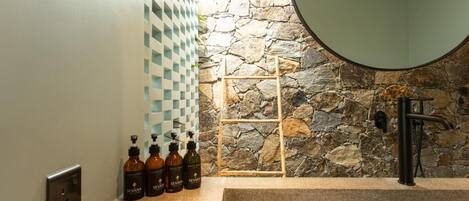 A bathroom with a stone wall, a checkered wall panel, a sink, and several bottles of Sevana products.