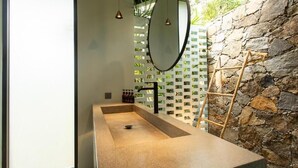 A modern bathroom with a rectangular sink, a large mirror, and a stone wall. - The Sevana (Matara)