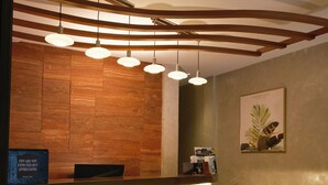 Un comptoir d’accueil d’hôtel avec un mur revêtu de panneaux en bois, une enseigne indiquant « J Boutique Hotel » et une estampe botanique encadrée accrochée au mur.
