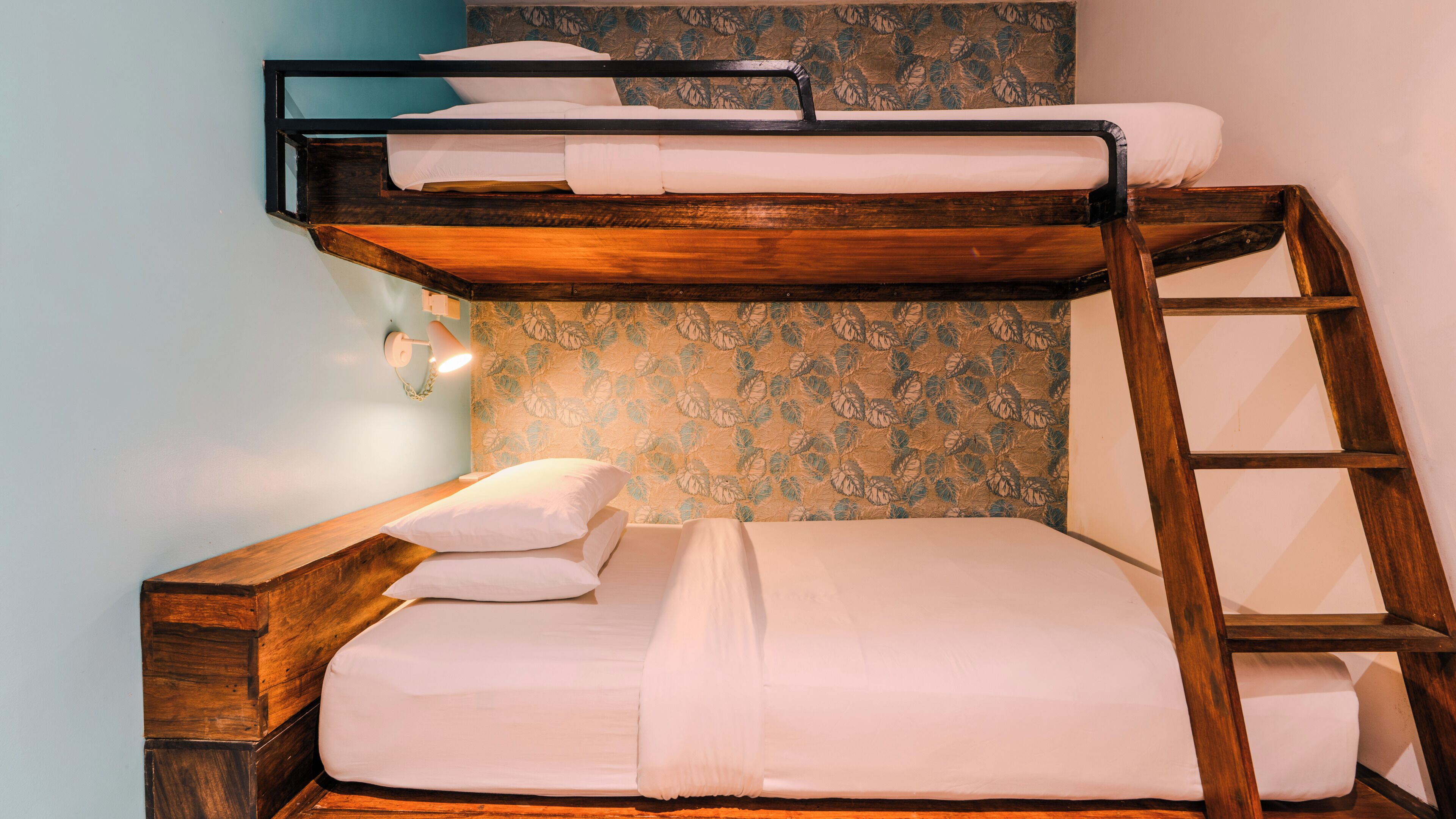 A bunk bed with a wooden ladder, a wall-mounted light, and a floral-patterned wallpaper.