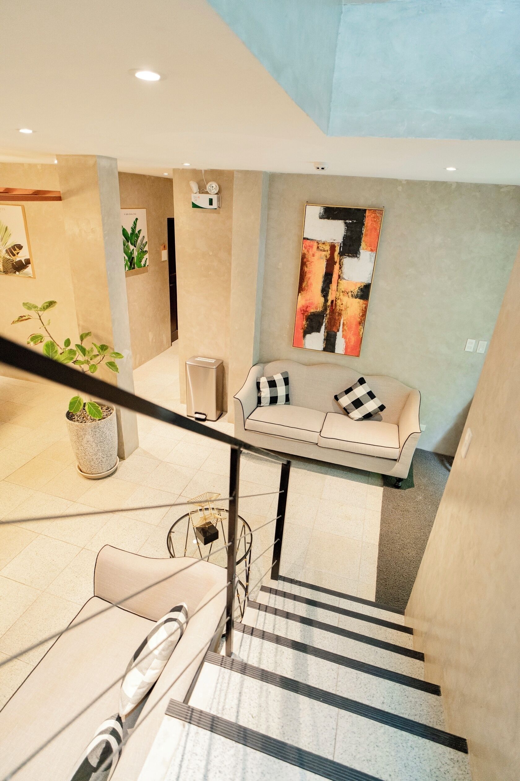Un interior moderno con una escalera, un sofá con cojines cuadriculados, una mesa de centro y un cuadro en la pared.