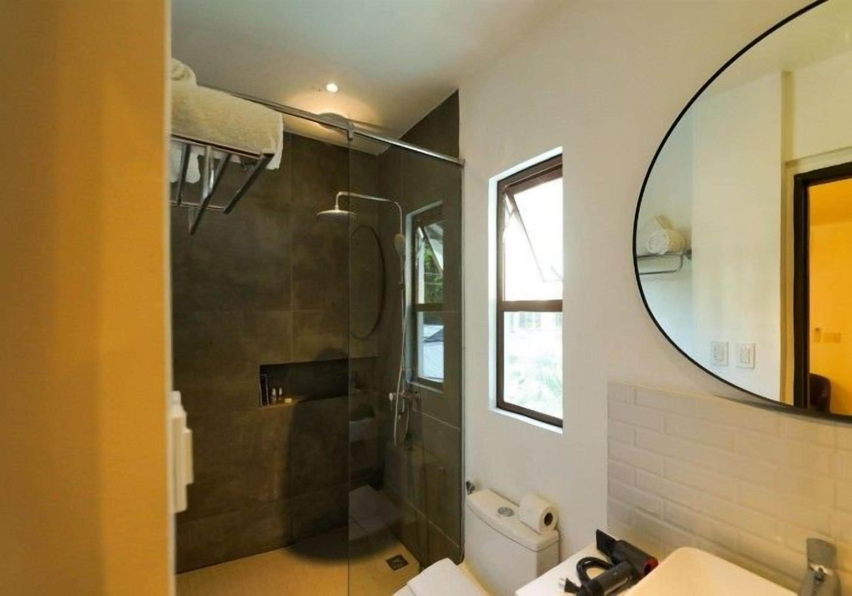 Un baño moderno con ducha de vidrio, un espejo grande y una ventana que proporciona luz natural.