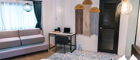 A modern hotel room with a bed, a desk, a sofa, and a large window with curtains.