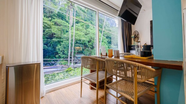 Une chambre moderne dotée d’une grande fenêtre, d’une table à manger avec des chaises, d’un petit réfrigérateur et d’un téléviseur fixé au mur.