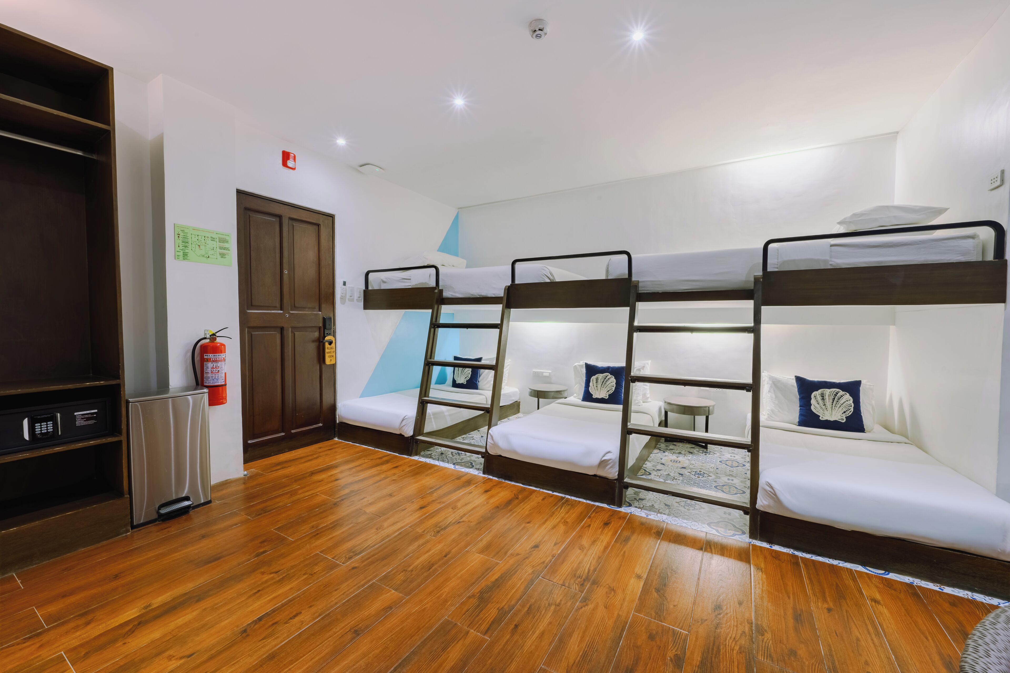 A bunk room with wooden flooring, a fire extinguisher, a small table, and a wardrobe.