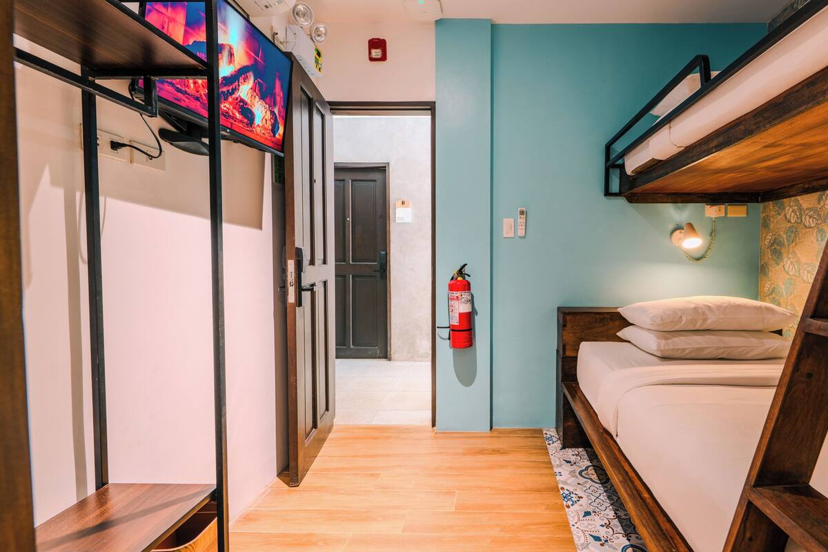 A room with bunk beds, a fire extinguisher, a wall-mounted light, and a television.