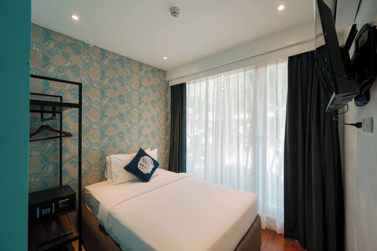 A hotel room with a bed, a TV, a desk with a remote, and a window with curtains.