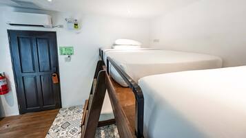 Een kamer met een bed, een deur, een airconditioner, een brandblusser en een klein apparaat aan de muur.