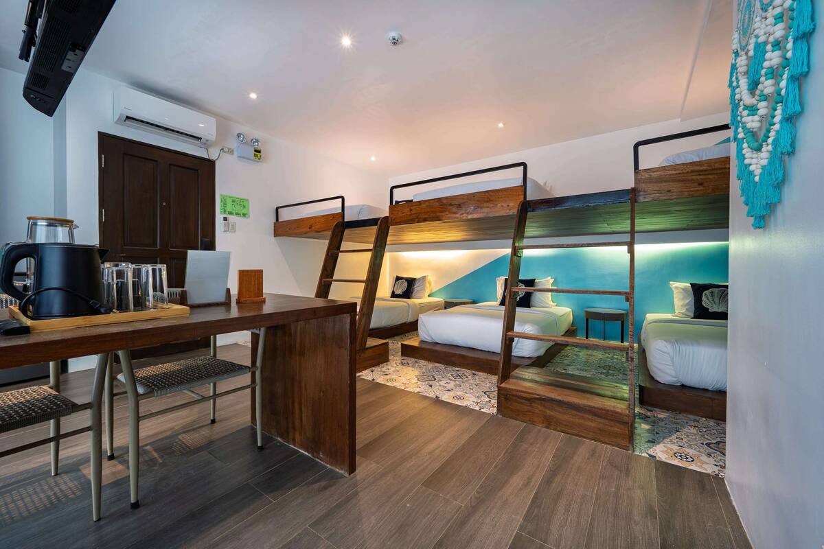 A compact hotel room with bunk beds, a kitchenette, a wooden desk, and a patterned rug.