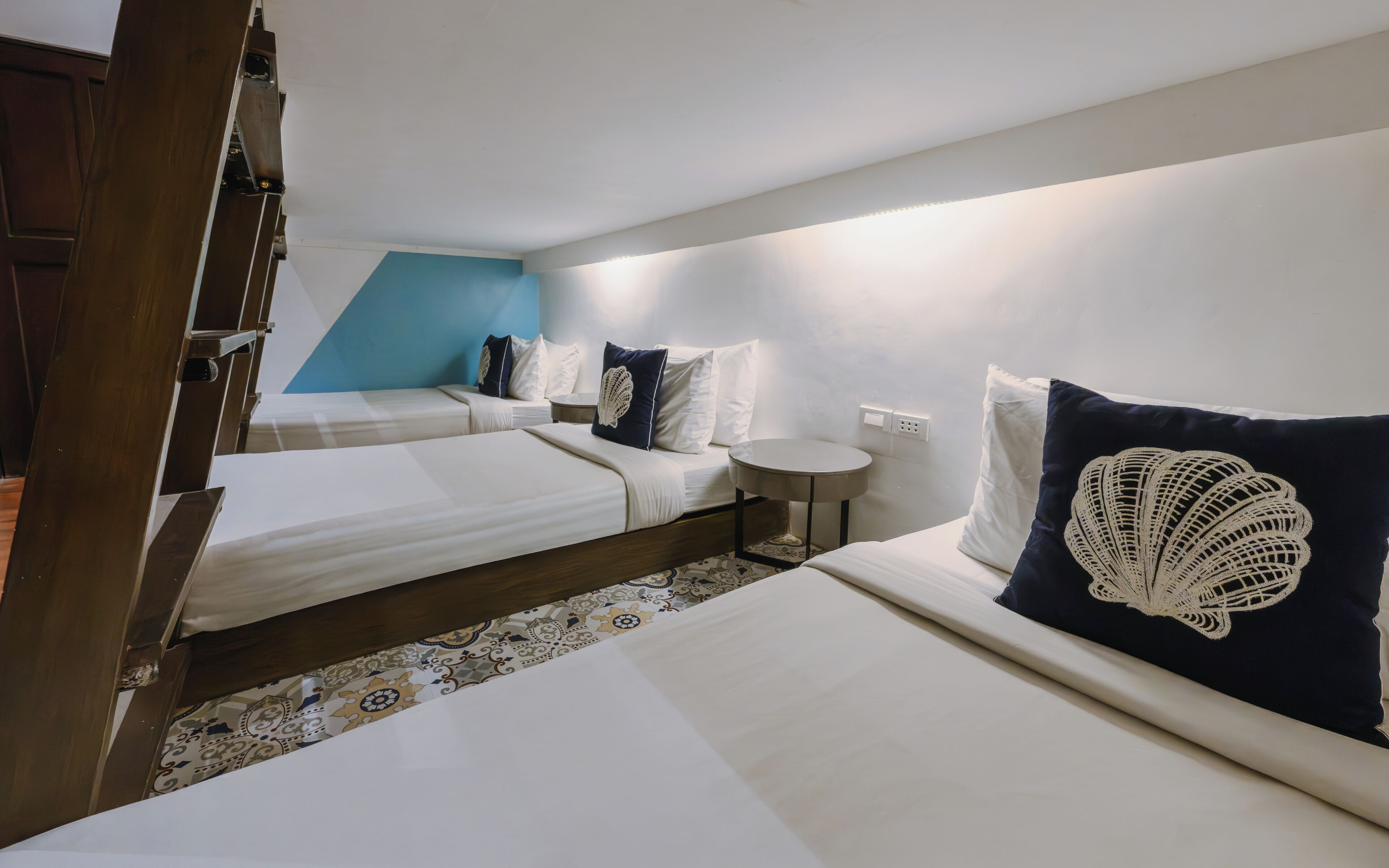 A hotel room with two beds, a small round table, and a blue accent wall.