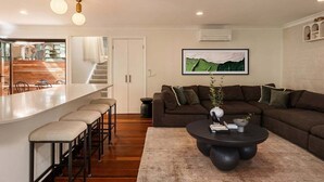 Un salon moderne avec un coin bar, un grand canapé d’angle marron, une table basse ronde et un tableau représentant un paysage, encadré, accroché au mur.