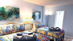 Un dormitorio con dos camas, cada una con una colcha de motivos de caballitos de mar, una mesita de noche con lámpara y obras de arte en las paredes.
