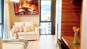 Een moderne slaapkamer met een slaapbank, nachtkastje, televisie en uitzicht op de stad door grote ramen.