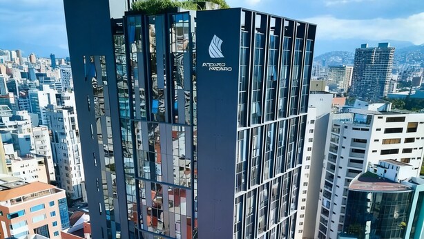 Een modern hoog gebouw met een glazen gevel, gelegen in een stedelijke omgeving met omliggende gebouwen.