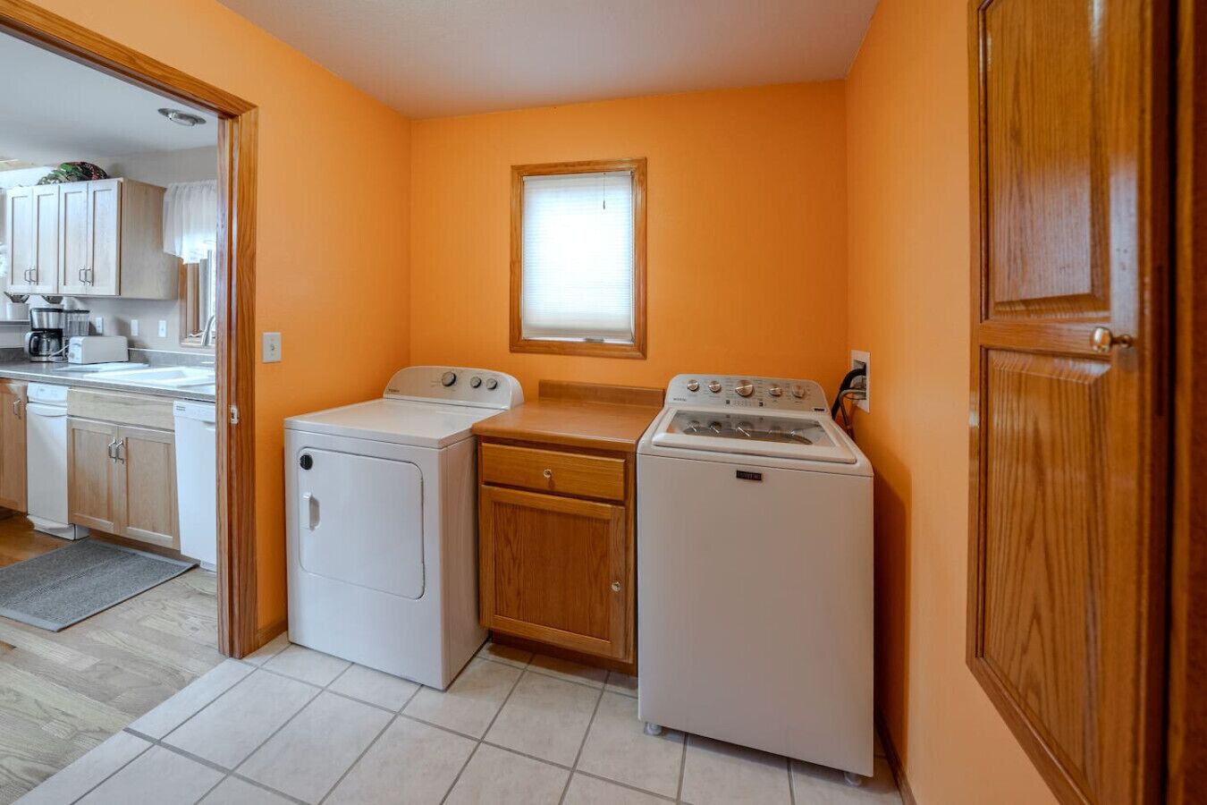 A compact kitchen with a washer and dryer, wooden cabinets, and a window.