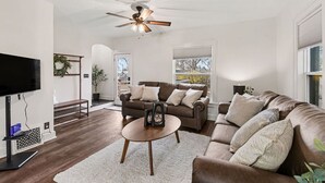 A living room with a brown leather sofa, a coffee table, a TV, and a ceiling fan. - Haven on Main - 4 Bed 2 Bath (Sioux Falls)