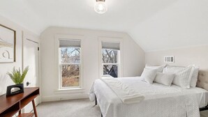 A bedroom with a large bed, two windows, a desk, and a plant. - Haven on Main - 4 Bed 2 Bath (Sioux Falls)