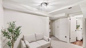 A modern, minimalist living room with a beige sofa, a potted plant, and a hallway leading to a bathroom. - Haven on Main - 4 Bed 2 Bath (Sioux Falls)