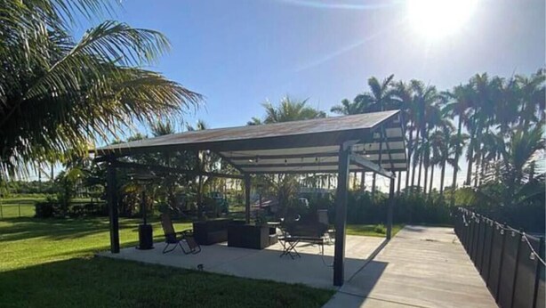 A covered outdoor seating area with tables and chairs, surrounded by a well-maintained lawn and palm trees. - 3-bedroom farmhouse in peaceful Miami with cool vibes (Miami)